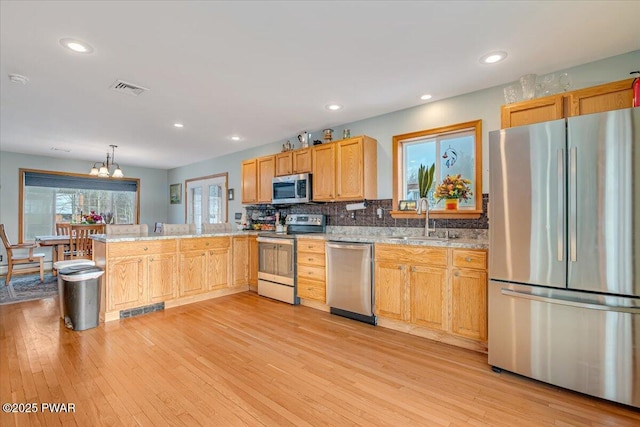 kitchen with light stone countertops, light wood-type flooring, stainless steel appliances, sink, and hanging light fixtures