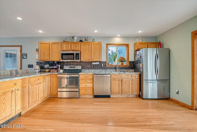 kitchen with light stone countertops, appliances with stainless steel finishes, light wood-type flooring, decorative backsplash, and sink