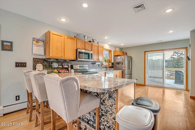 kitchen with a kitchen bar, kitchen peninsula, tasteful backsplash, stainless steel appliances, and light hardwood / wood-style flooring