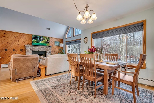 dining area with a baseboard radiator, an inviting chandelier, a healthy amount of sunlight, and wood walls