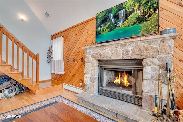 interior details with baseboard heating, a stone fireplace, wooden walls, and hardwood / wood-style flooring