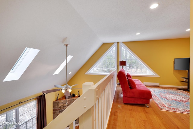 living area featuring ceiling fan, vaulted ceiling with skylight, a baseboard radiator, and wood-type flooring