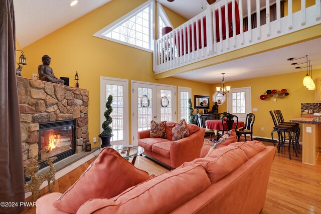 living room with high vaulted ceiling, french doors, a fireplace, a notable chandelier, and light hardwood / wood-style floors