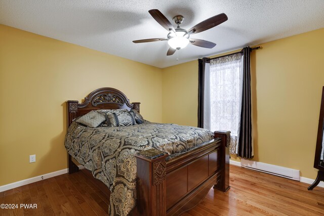 bedroom with ceiling fan, light hardwood / wood-style floors, a textured ceiling, and a baseboard heating unit