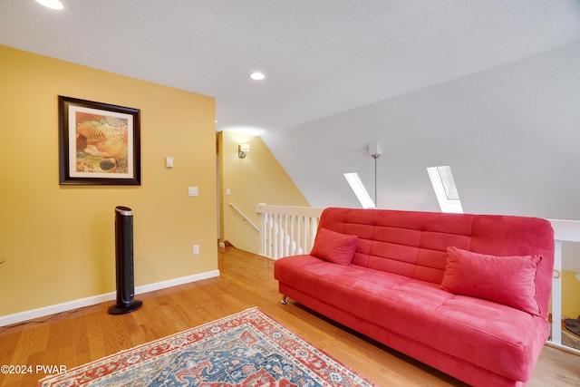 living room featuring hardwood / wood-style flooring, lofted ceiling with skylight, and a textured ceiling