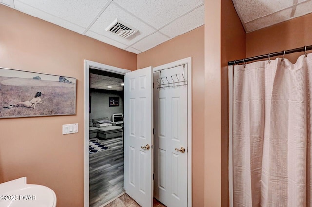 bathroom with a drop ceiling, toilet, a shower with shower curtain, wood finished floors, and visible vents