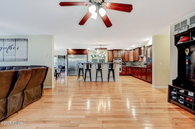 living room with baseboards, ceiling fan, and light wood finished floors