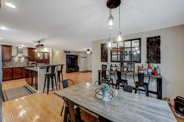 dining area with a bar, light wood-style flooring, and ceiling fan