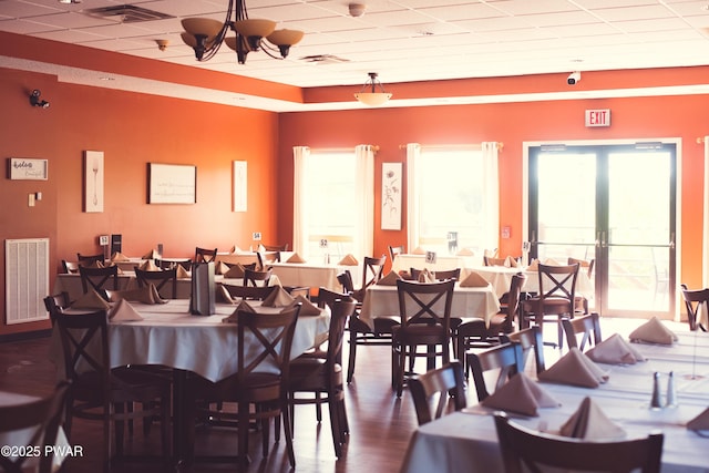 dining space featuring visible vents, a drop ceiling, wood finished floors, an inviting chandelier, and french doors