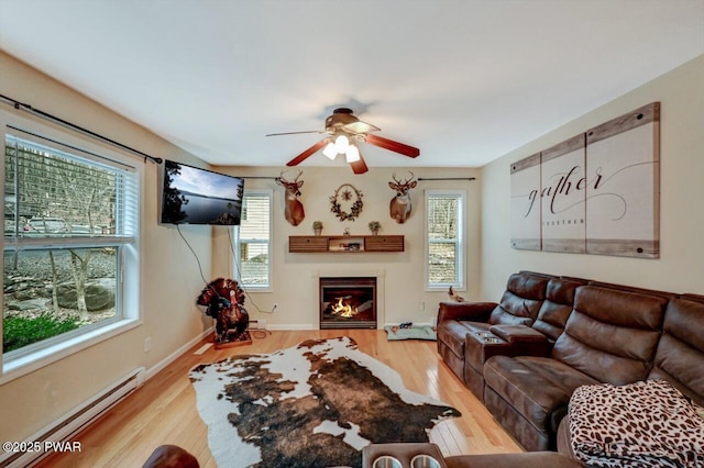 living room with a glass covered fireplace, a healthy amount of sunlight, baseboard heating, and wood finished floors