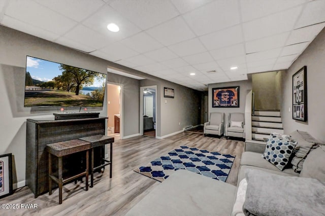 living room with a paneled ceiling, wood finished floors, and stairs