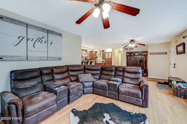 living room featuring ceiling fan with notable chandelier, wood finished floors, and baseboards