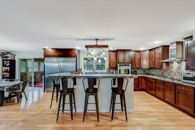 kitchen featuring light wood-style flooring, backsplash, appliances with stainless steel finishes, dark stone counters, and wall chimney exhaust hood