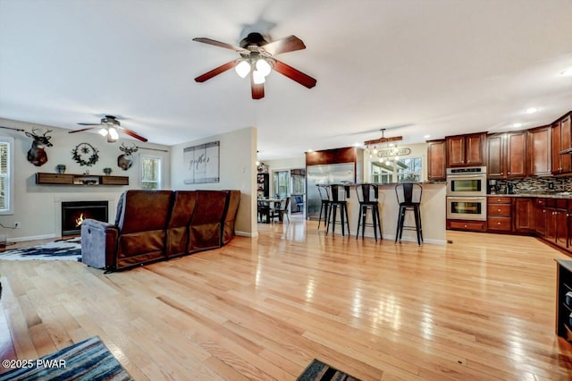 living area featuring light wood-type flooring, a lit fireplace, baseboards, and a ceiling fan