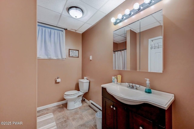 bathroom with a drop ceiling, toilet, a baseboard heating unit, vanity, and baseboards