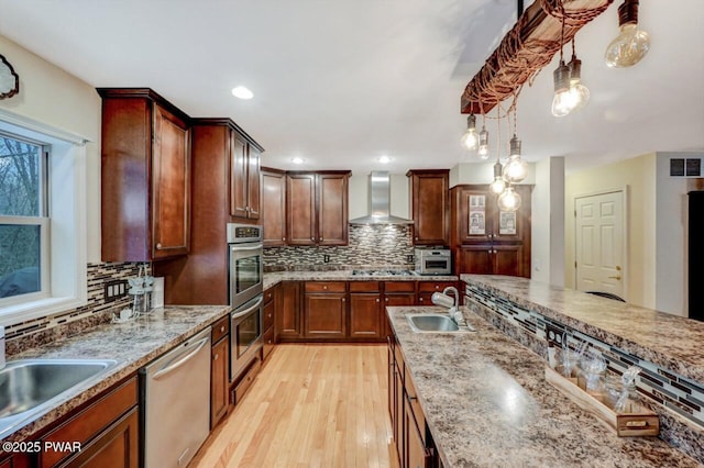 kitchen with a sink, visible vents, wall chimney range hood, appliances with stainless steel finishes, and light wood finished floors