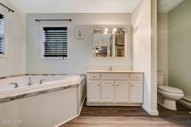 bathroom featuring toilet, wood finished floors, vanity, a baseboard heating unit, and a bath