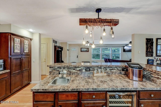 kitchen featuring light wood-style flooring, wine cooler, a center island, light stone countertops, and a sink