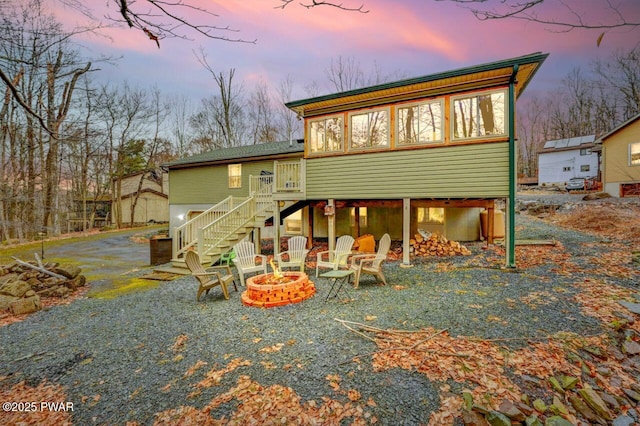 back of house featuring stairs, an outdoor fire pit, and a sunroom