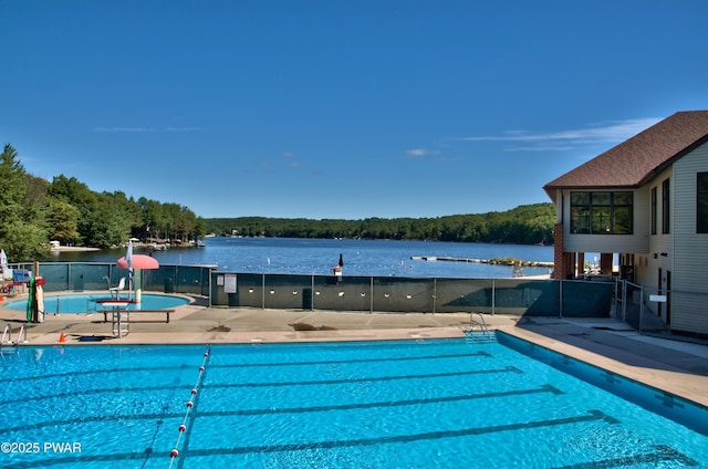 pool with a water view, a patio, a wooded view, and fence