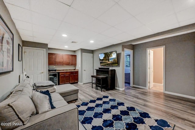 living room with beverage cooler, baseboards, a paneled ceiling, light wood-type flooring, and recessed lighting