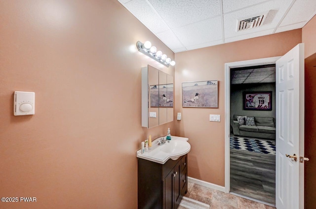 bathroom with a paneled ceiling, vanity, visible vents, and baseboards