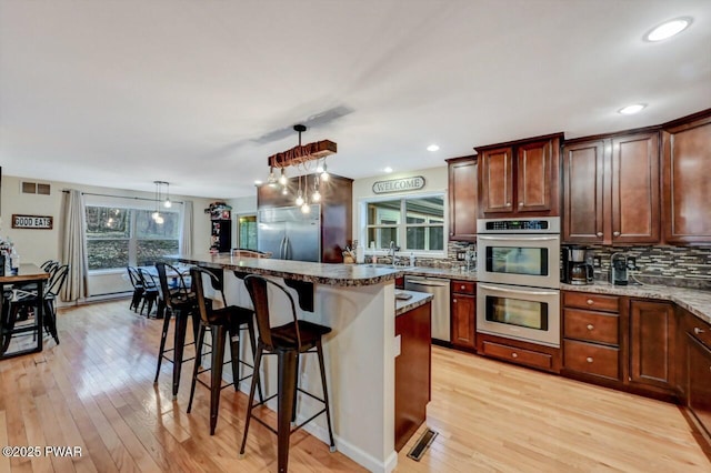 kitchen featuring light wood-type flooring, a breakfast bar area, stainless steel appliances, and decorative backsplash