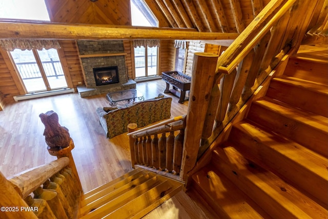 staircase with a stone fireplace, hardwood / wood-style floors, log walls, and high vaulted ceiling