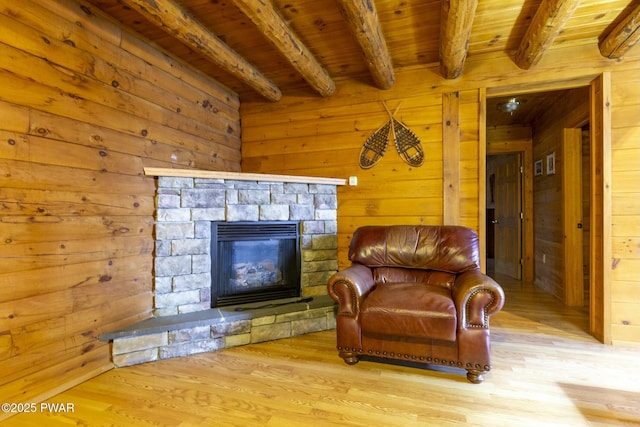 living area featuring beam ceiling, wooden ceiling, wood walls, a fireplace, and light wood-type flooring