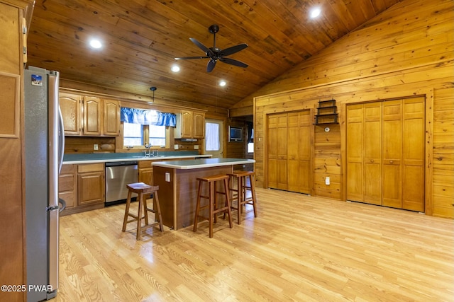 kitchen with a center island, hanging light fixtures, wooden walls, appliances with stainless steel finishes, and a breakfast bar area