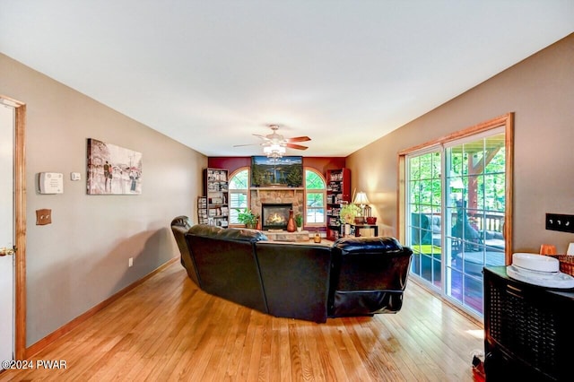 living room featuring a stone fireplace, ceiling fan, and light hardwood / wood-style floors