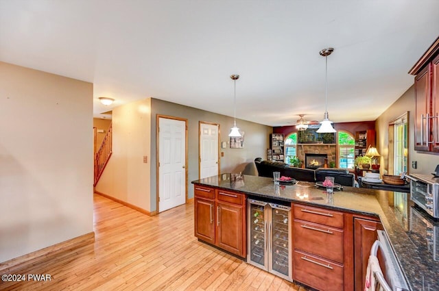 kitchen featuring light wood-type flooring, ceiling fan, dark stone countertops, wine cooler, and hanging light fixtures