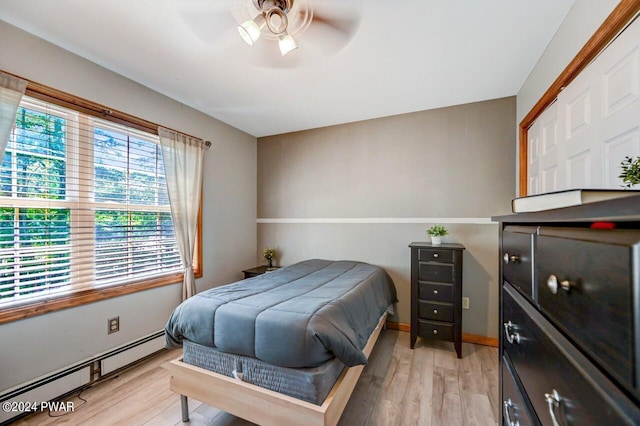 bedroom with a closet, light hardwood / wood-style flooring, ceiling fan, and a baseboard heating unit