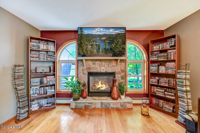 living area featuring wood-type flooring, a baseboard radiator, and a stone fireplace