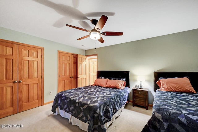 bedroom featuring ceiling fan, light colored carpet, and multiple closets