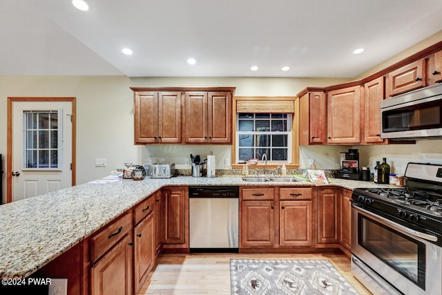 kitchen with appliances with stainless steel finishes, light hardwood / wood-style floors, light stone counters, and sink