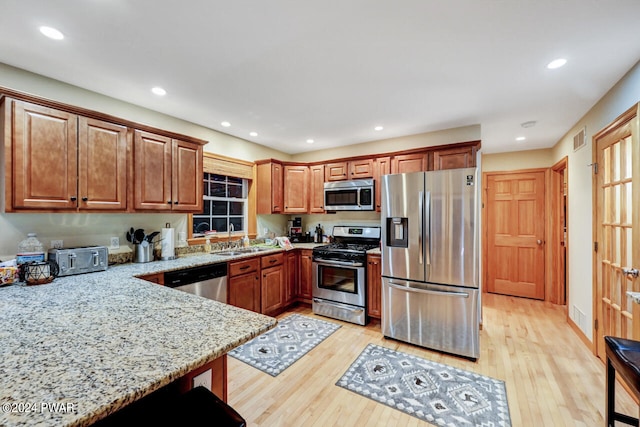 kitchen featuring sink, light stone counters, light wood-type flooring, and stainless steel appliances