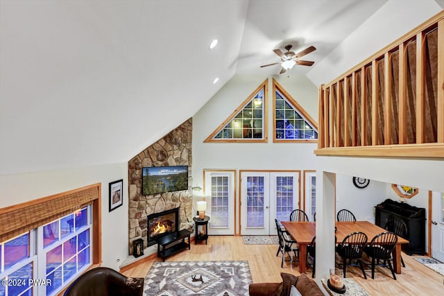 living room with lofted ceiling, french doors, a stone fireplace, ceiling fan, and light wood-type flooring