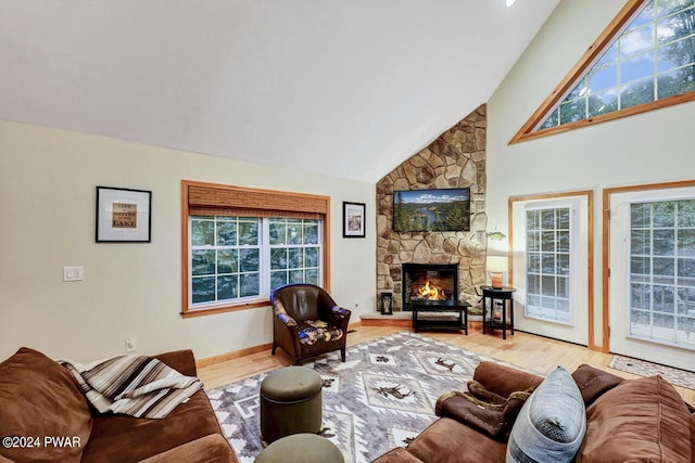 living room with a stone fireplace, high vaulted ceiling, and light hardwood / wood-style flooring