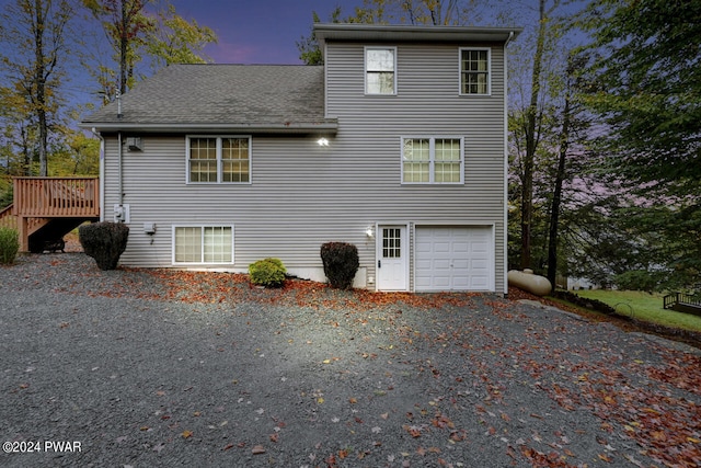 back house at dusk featuring a garage and a wooden deck