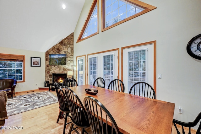 dining area featuring a fireplace, light wood-type flooring, and high vaulted ceiling