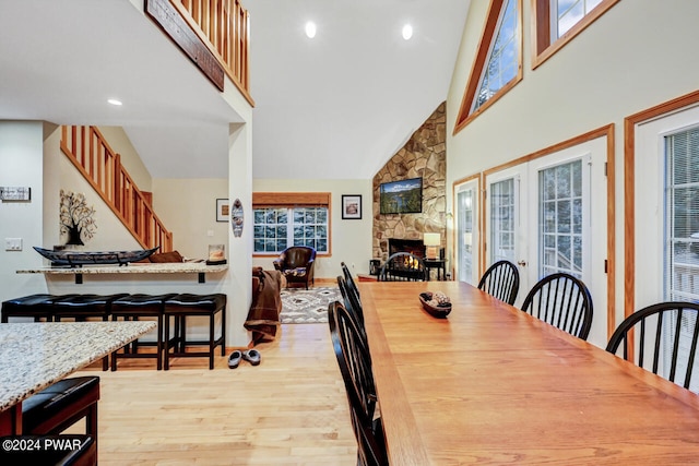 dining area with a fireplace, high vaulted ceiling, and light hardwood / wood-style flooring