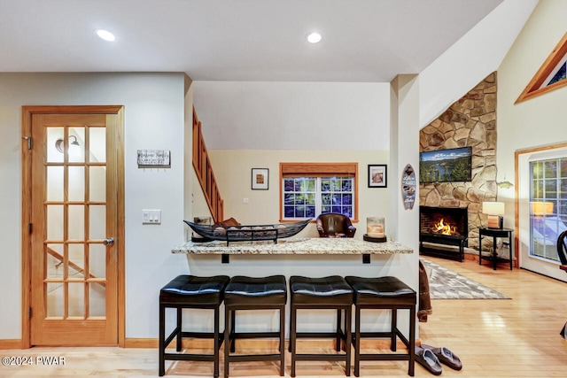 kitchen with light stone countertops, kitchen peninsula, light hardwood / wood-style floors, a fireplace, and a breakfast bar