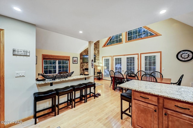 kitchen featuring a breakfast bar area, light stone countertops, french doors, and vaulted ceiling