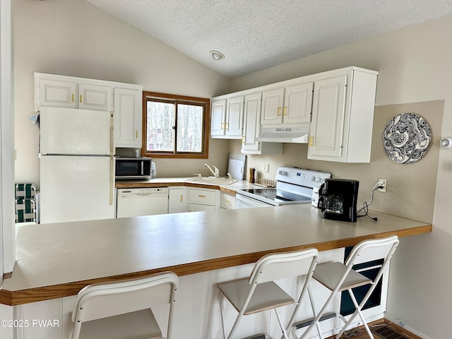 kitchen featuring white appliances, a sink, under cabinet range hood, vaulted ceiling, and a peninsula