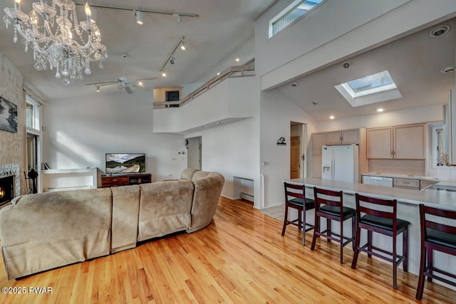 living room with high vaulted ceiling, a fireplace, a skylight, baseboard heating, and light wood-type flooring