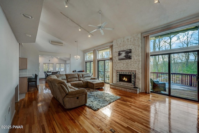 living room with ceiling fan with notable chandelier, a stone fireplace, hardwood / wood-style floors, and rail lighting