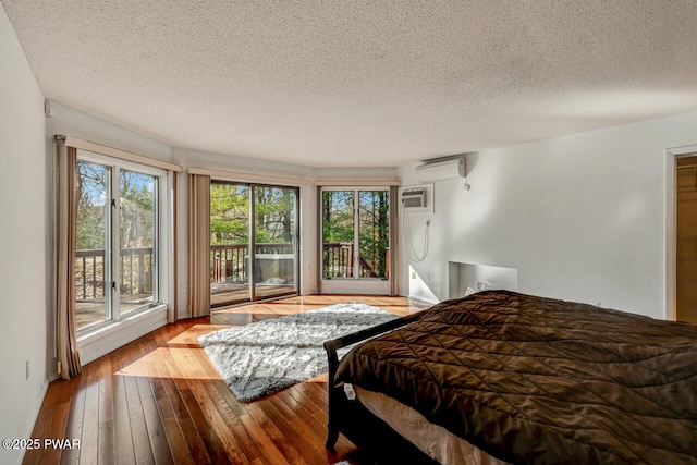 bedroom with a wall unit AC, access to exterior, light hardwood / wood-style flooring, and a textured ceiling