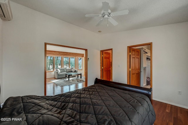 bedroom featuring wood-type flooring, a wall mounted air conditioner, ceiling fan, and a textured ceiling