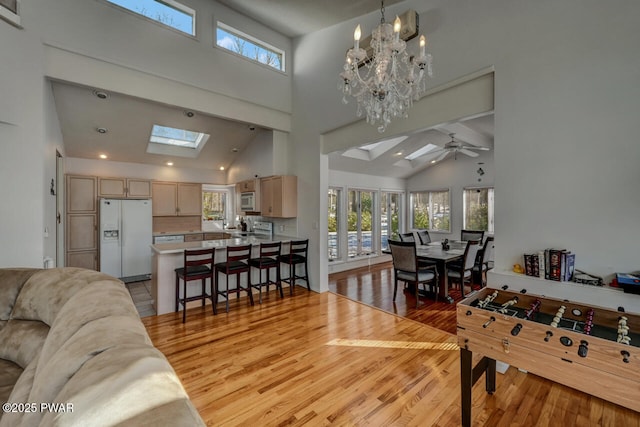 interior space with light hardwood / wood-style floors, ceiling fan with notable chandelier, high vaulted ceiling, and a skylight